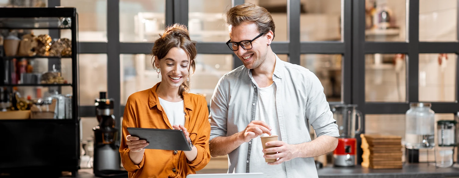 casal sorridente num café, ela com tablet na mão e ele com chávena na mão