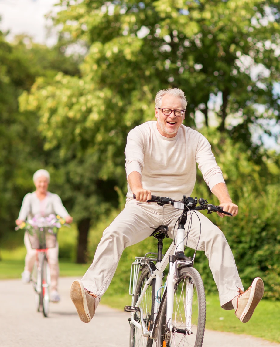 casal a andar de bicicleta, com ar divertido, num caminho de um parque verde