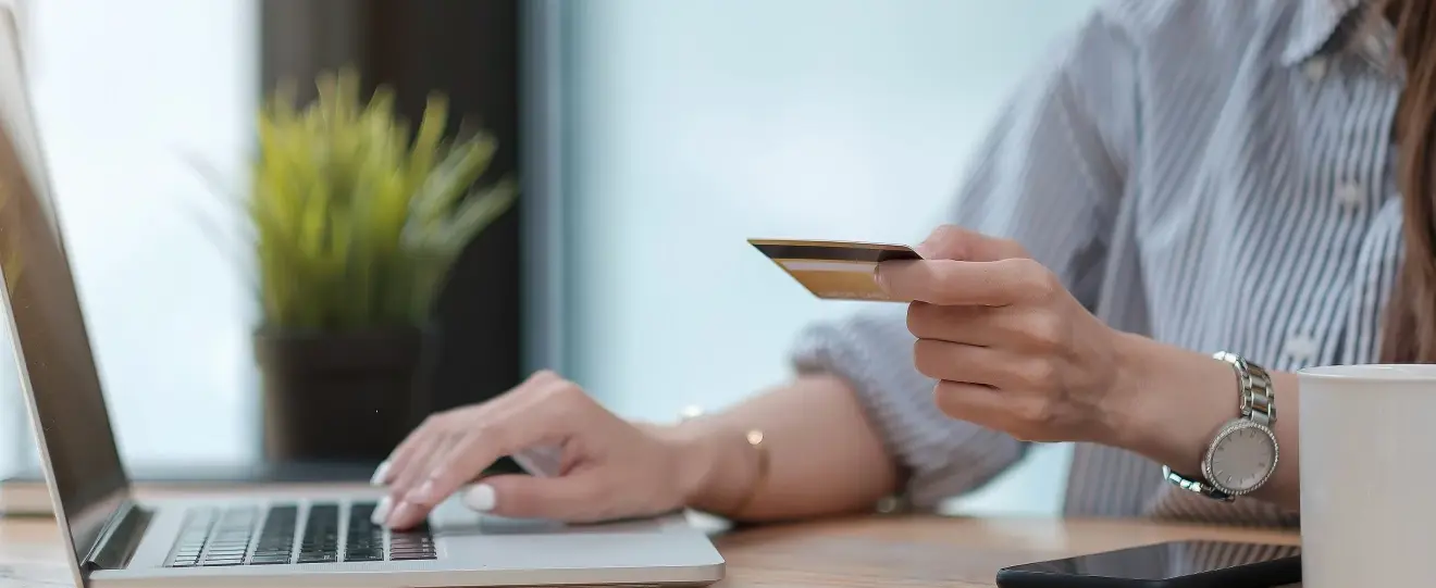 Mão a segurar um cartão de crédito sobre um teclado de computador portátil