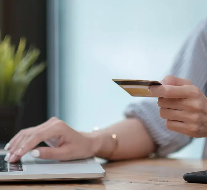 Mão a segurar um cartão de crédito sobre um teclado de computador portátil