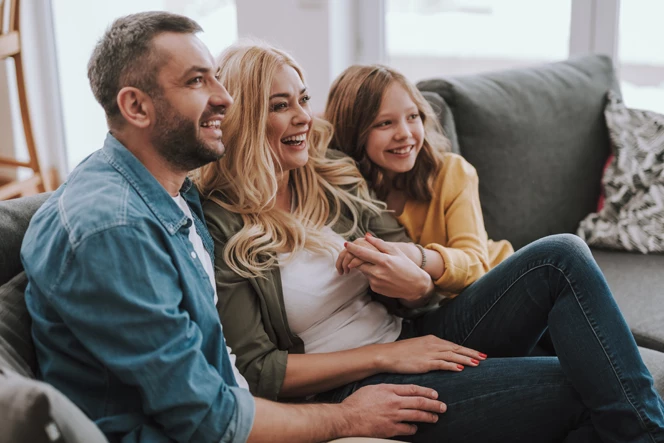 casal e filha pequena sorridentes, num sofá, num momento de cumplicidade