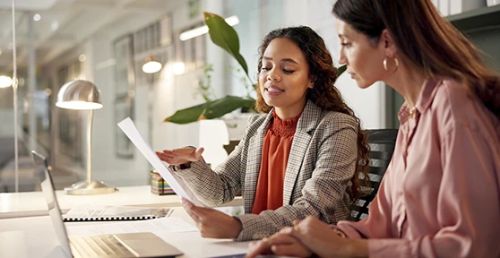 2  mulheres num escritório, uma com papel na mão, a conversar