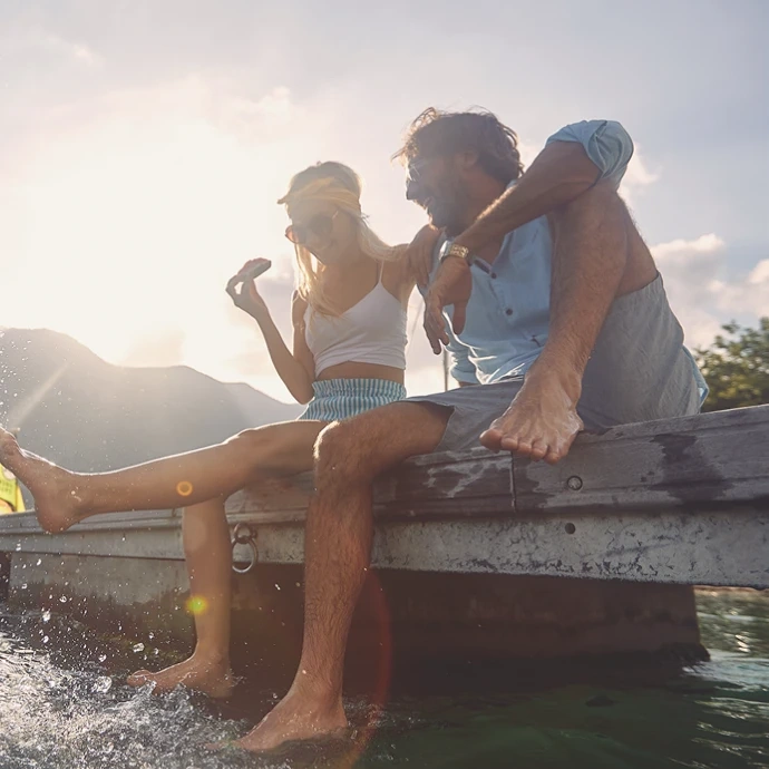 Couple sitting on the edge of a boat with their feet in the water at sunset