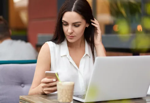 senhora numa esplanada de café, com telemóvel e computador portátil