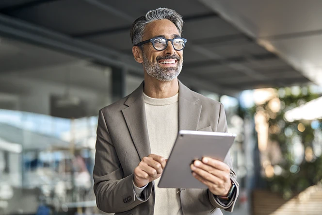 Grey-haired man with glasses, outside a building, holding a tablet