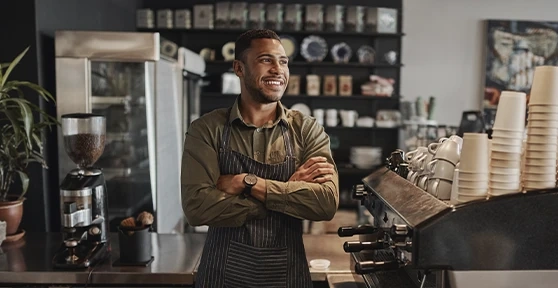 Dono de um café sorridente de braços cruzados no seu estabelecimento