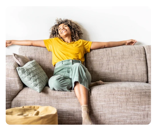 Mulher relaxa no sofá com braços abertos e expressão feliz