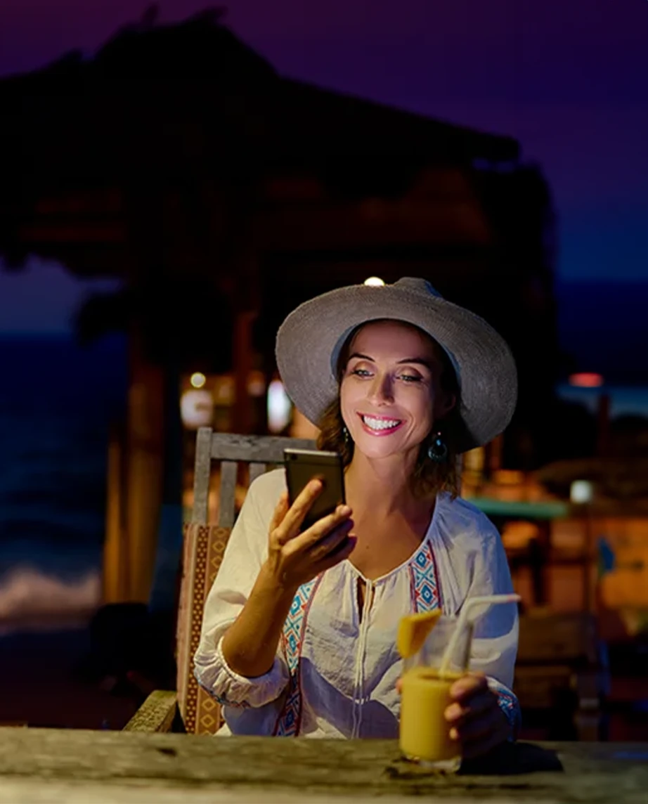 woman sitting at a café table outside, at night, smiling with a phone in her hand