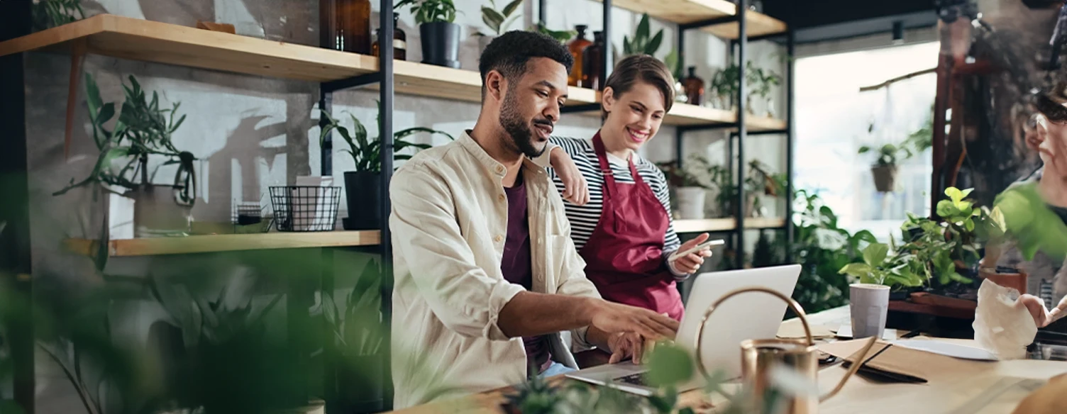 young couple consulting a computer placed on a countertop, surrounded by plants