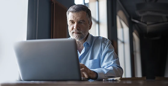 Homem de barba a trabalhar concentrado num computador portátil