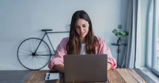 Mulher a trabalhar no portátil em mesa de madeira com bicicleta ao fundo
