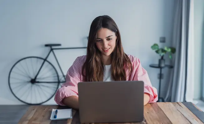 Mulher a trabalhar no portátil em mesa de madeira com bicicleta ao fundo