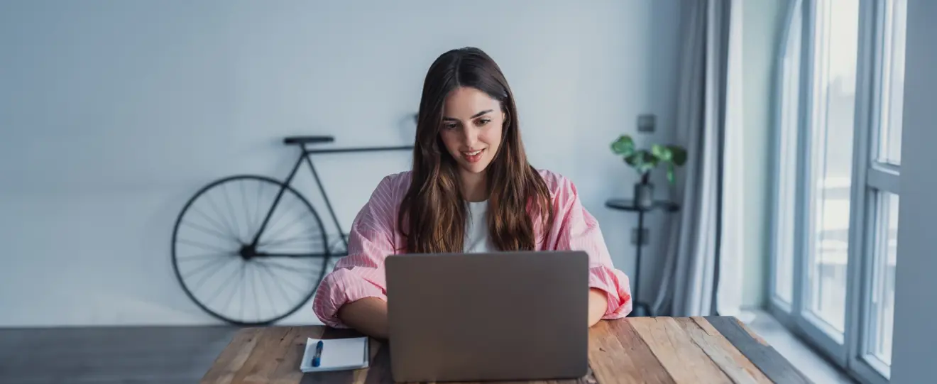 Mulher a trabalhar no portátil em mesa de madeira com bicicleta ao fundo