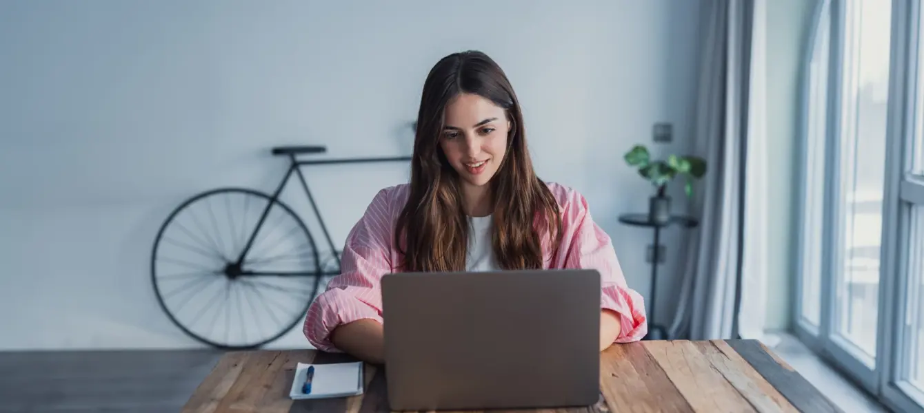 Mulher a trabalhar no portátil em mesa de madeira com bicicleta ao fundo