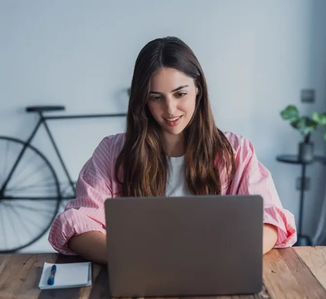 Mulher a trabalhar no portátil em mesa de madeira com bicicleta ao fundo