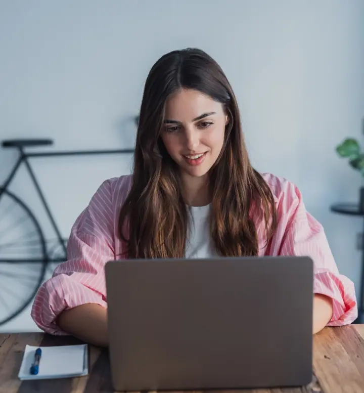 Mulher a trabalhar no portátil em mesa de madeira com bicicleta ao fundo