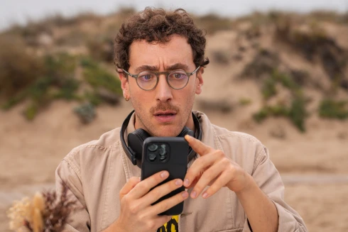 Ator, a representar a personagem Diogo Pinto, a olhar para o seu telemóvel com um ar surpreendido