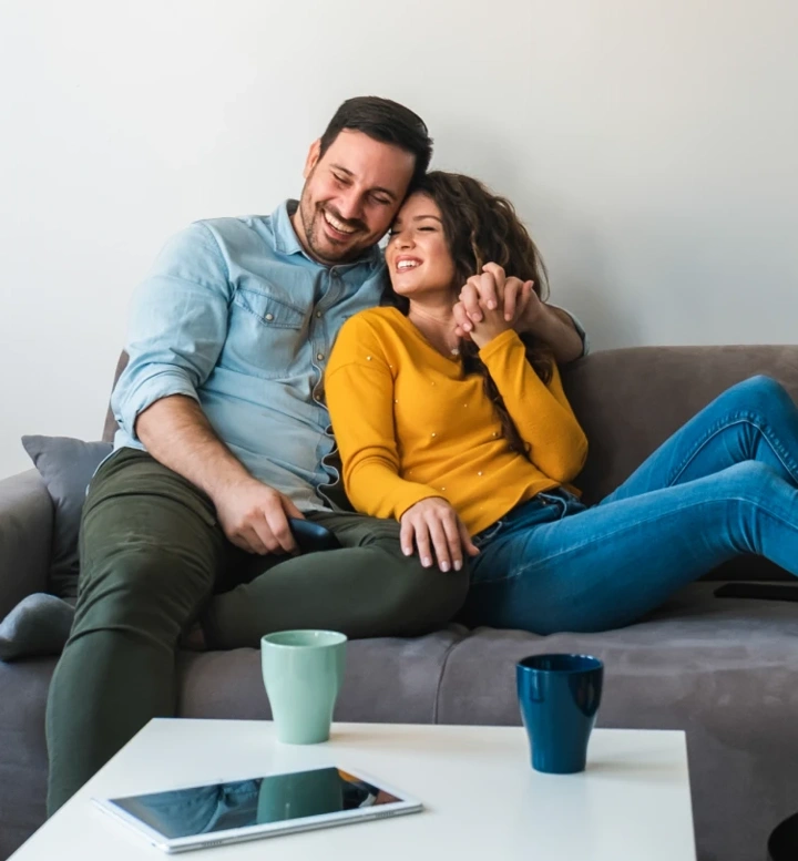 Casal sorridente relaxa no sofá da sala de estar
