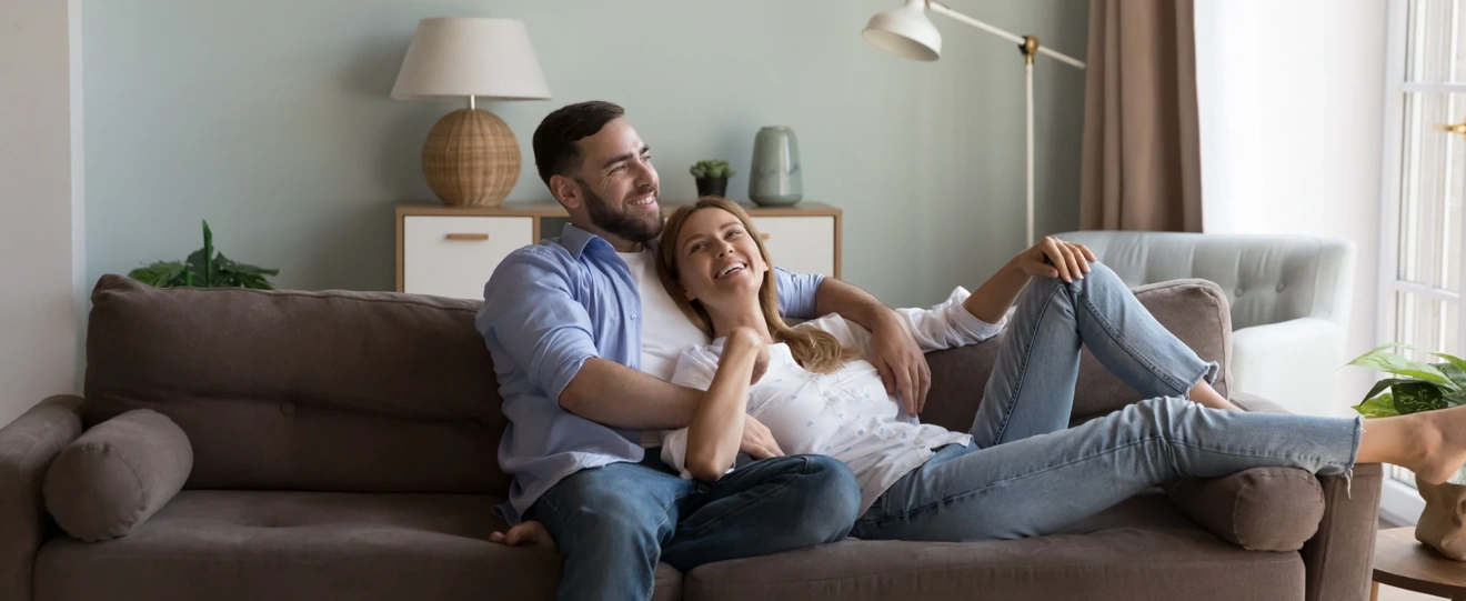 Casal sorridente relaxa no sofá da sala de estar