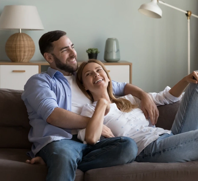 Casal sorridente relaxa no sofá da sala de estar