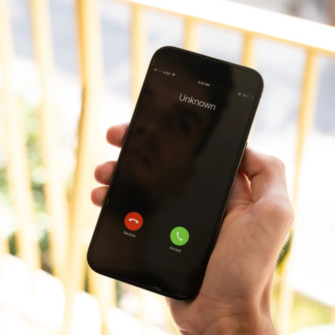 Mão direita a segurar num smartphone com uma chamada de um número desconhecido