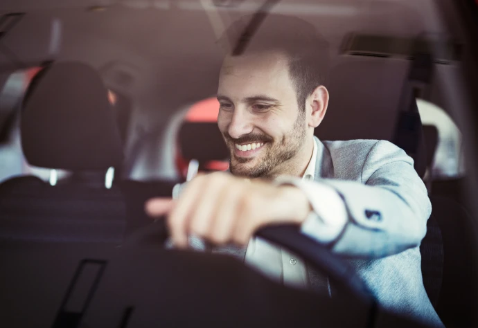 Homem de camisa branca e blazer cinza ao volante de um carro a sorrir para o tablier