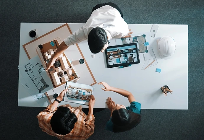 Vista de cima de dois arquitetos a discutir um projeto com plantas e uma maqueta