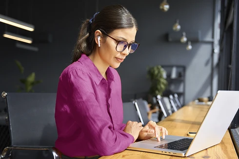 senhora sentada, com mesa de madeira corrida à frente, onde tem o seu computador