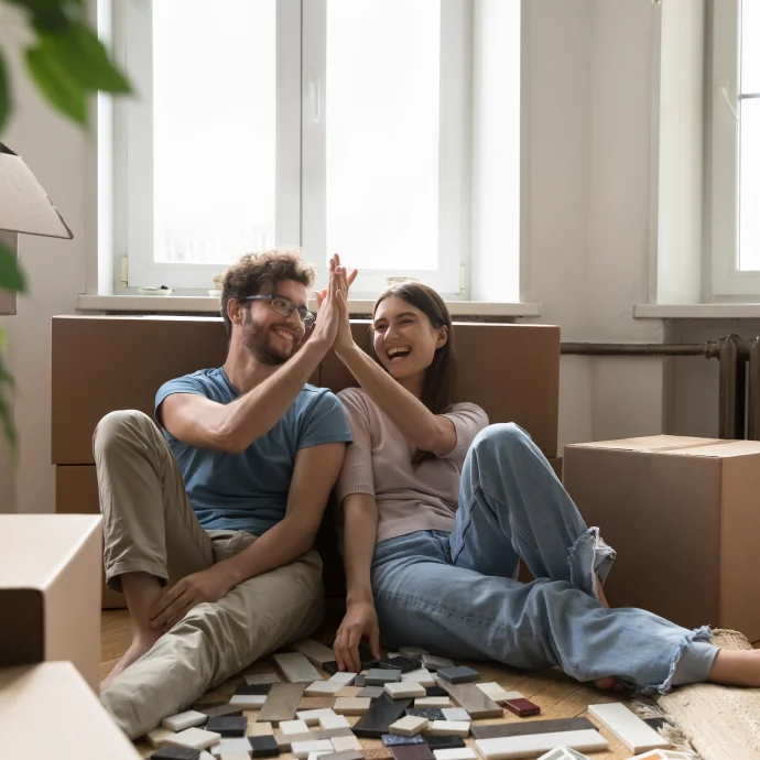Couple giving a high five while sitting on the floor, leaning against moving boxes