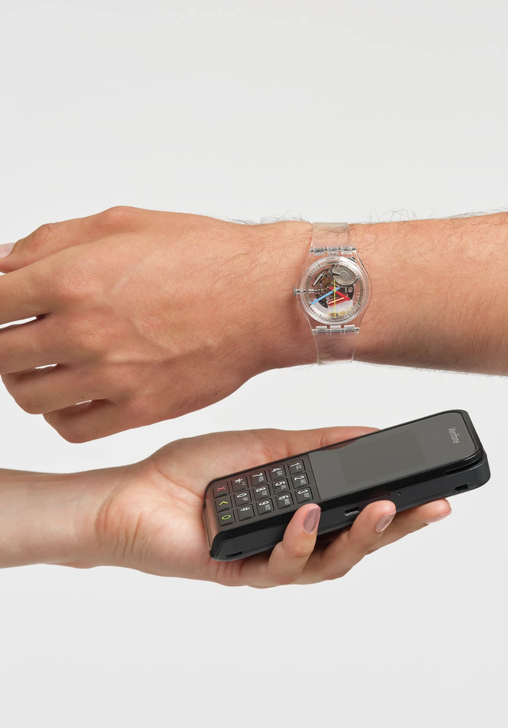A hand with an analog watch, approaching a mobile phone