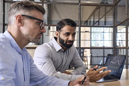 Dois colegas, no local de trabalho, com o computador aberto, a conversarem sobre Depósitos Estruturados