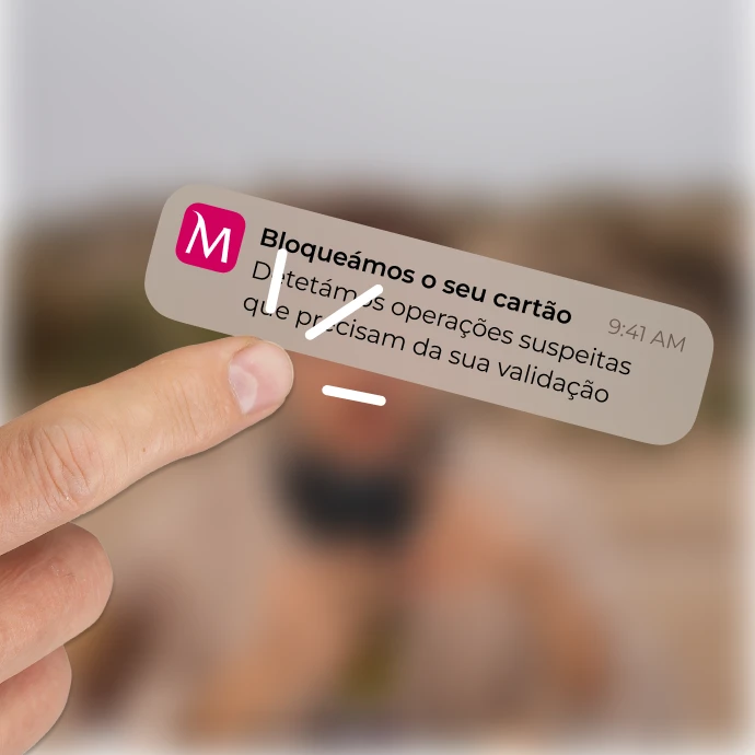 Dedo indicador a clicar numa notificação da App Millennium que diz "Bloqueámos o seu cartão. Detetámos operações suspeitas que precisam da sua validação"