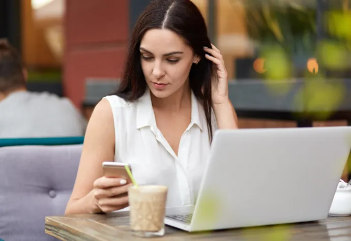 senhora numa esplanada de café, com telemóvel e computador portátil