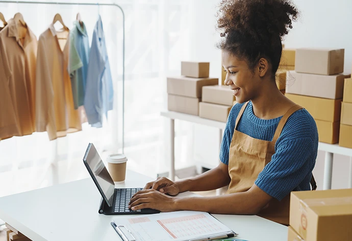 senhora sorridente ao computador, num atelier de roupa