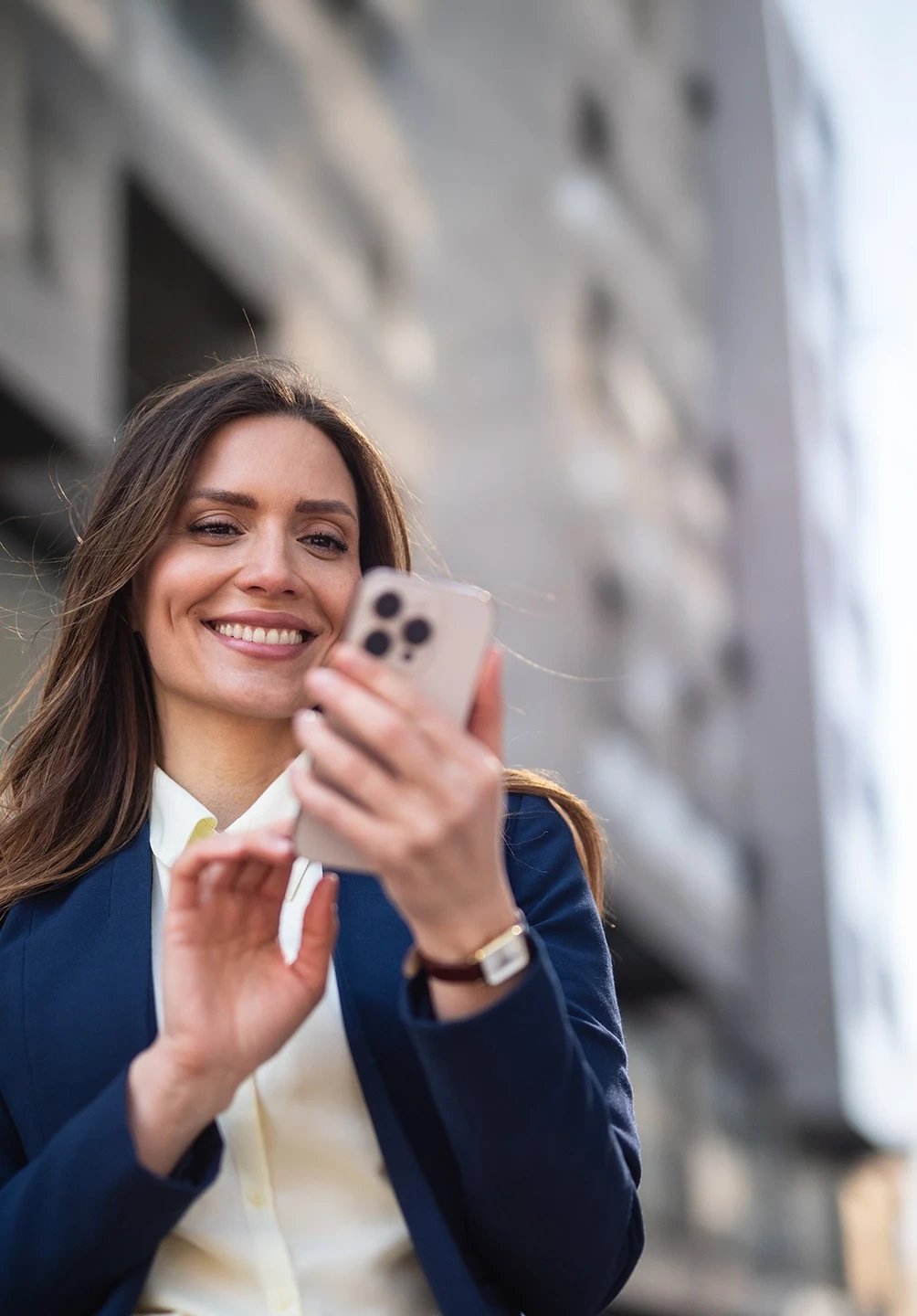 Woman in a suit smiles while using her mobile phone outdoors