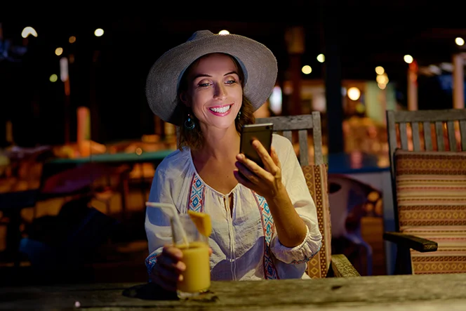 woman sitting at a café table outside, at night, smiling with a phone in her hand