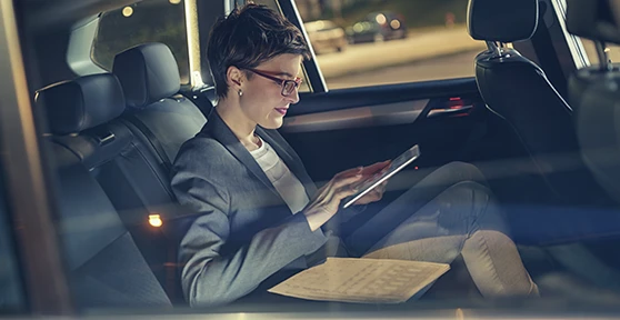 senhora, passageira no banco traseiro de um carro, com tablet na mão