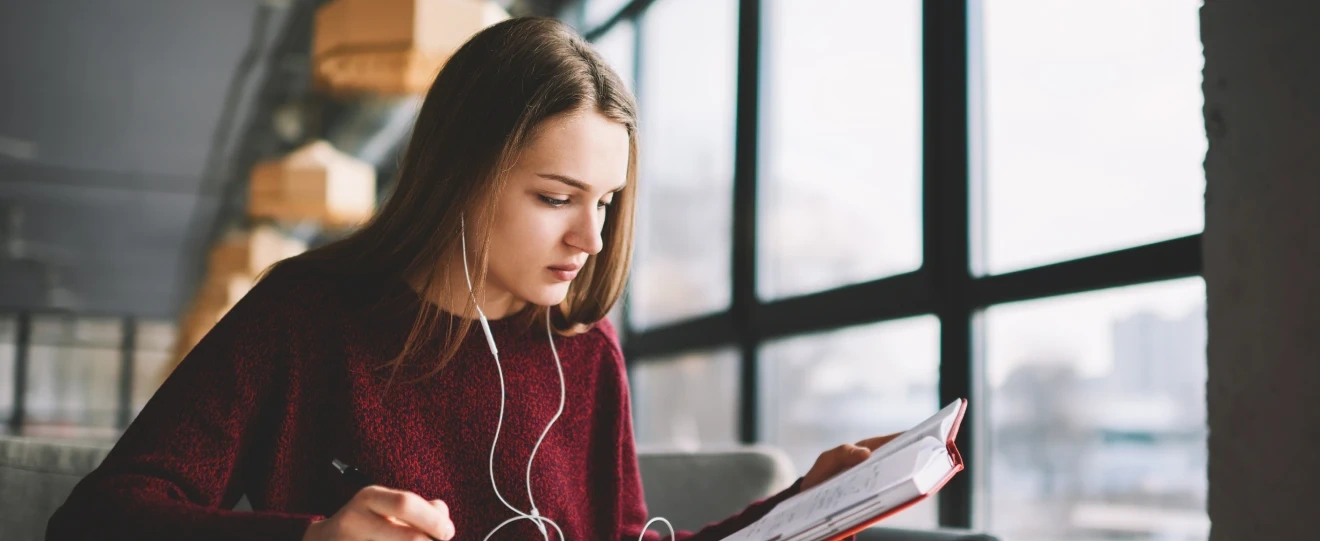 Jovem com auscultadores a estudar e a escrever num caderno