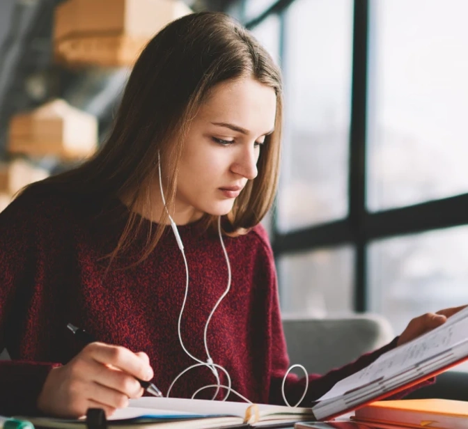 Jovem com auscultadores a estudar e a escrever num caderno