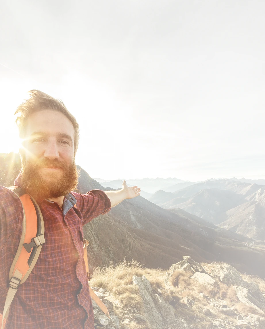 homem de barba, no topo de uma montanha, de braços abertos