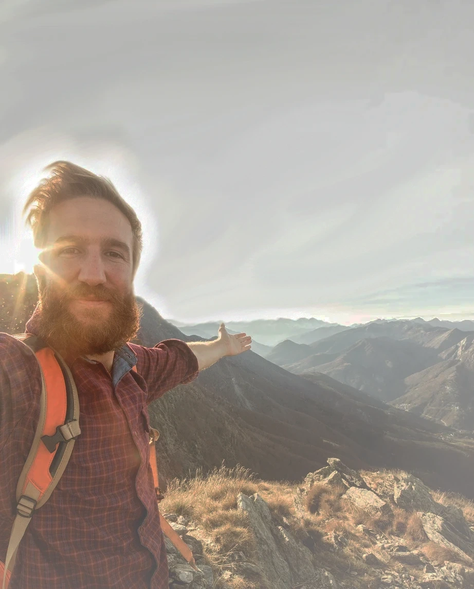 homem de barba, no topo de uma montanha, de braços abertos
