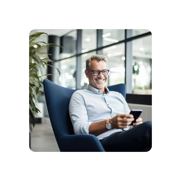 man sittig in a blue chair, smilling and holding phone