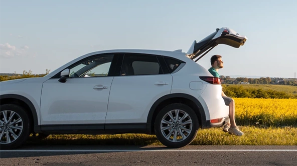  white car parked on the roadside, with the trunk open and a man sitting inside