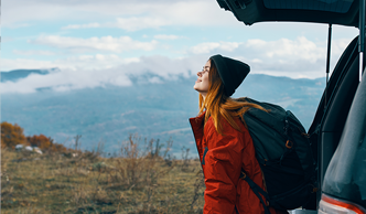 woman sitting in the open trunk of a car, on a landscape of mountains