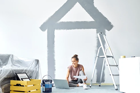 woman sitting on the floor in a house under renovation, with a laptop