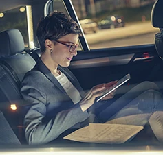 senhora, passageira no banco traseiro de um carro, com tablet na mão