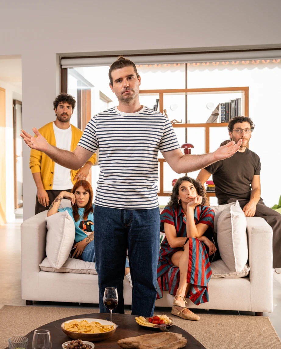 Filipe Ribeiro de braços abertos em frente a um grupo de amigos com ar aborrecido no sofá